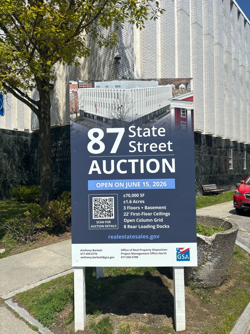 A sign in front of a building advertises an auction for 87 State Street on June 15, 2026, listing property details and contact information.