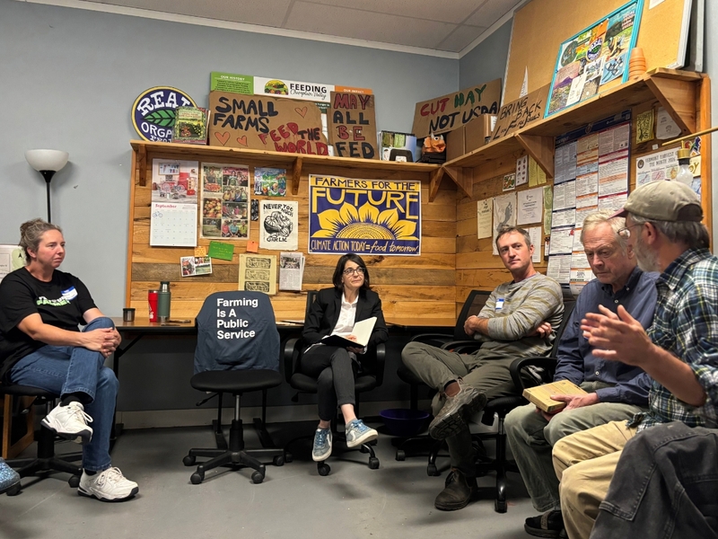 Five people sit in a room decorated with posters and signs about farming and food justice, having a discussion.