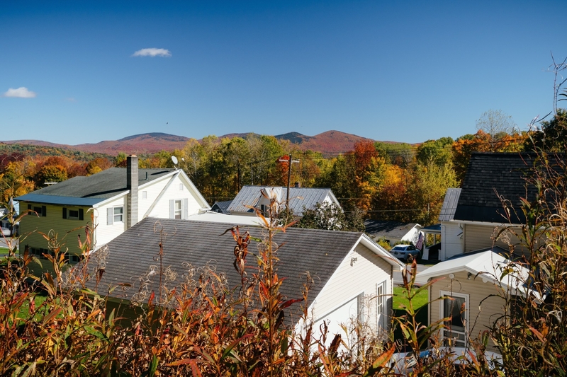 A residential neighborhood with houses and garages surrounded by autumn foliage, with mountains in the background.