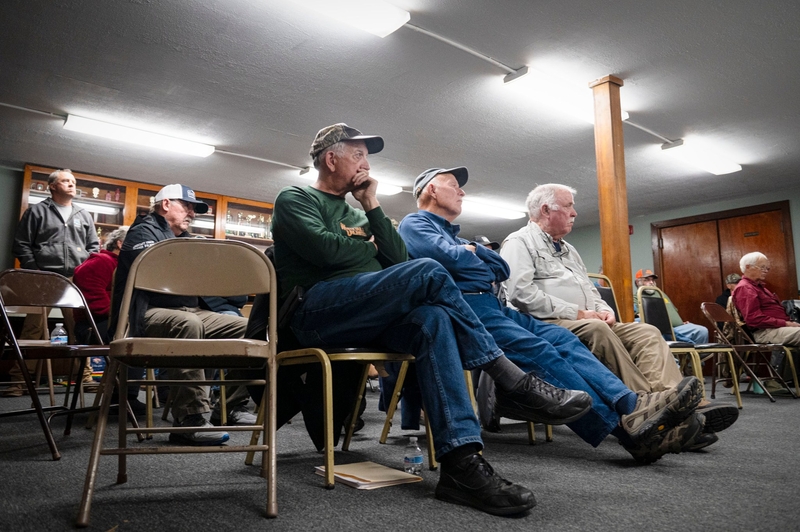 A row of men sitting on folding chairs at a meeting.