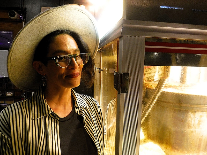 A person wearing a wide-brimmed hat and glasses stands next to a popcorn machine.