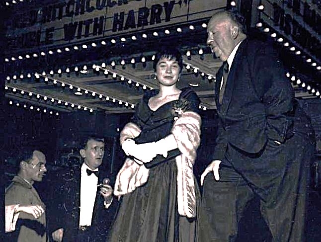 Alfred Hitchcock stands next to a woman in an evening gown and stole at a movie premiere for The Trouble with Harry.
