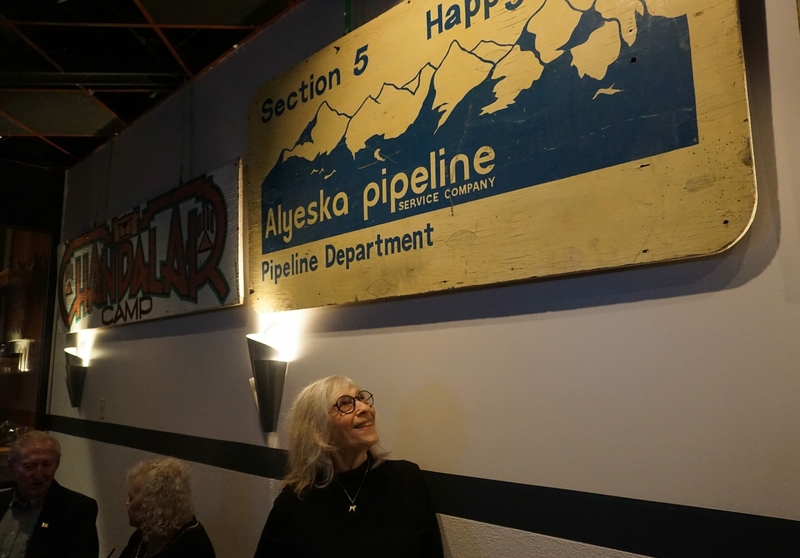 Nona Safra of Homer, attending an April 29, 2024, exhibit opening at the Petroleum Club of Anchorage, looks at a work camp sign that she found at a yard sale. The sign had been offered as scrap wood, she said. (Photo by Yereth Rosen/Alaska Beacon)