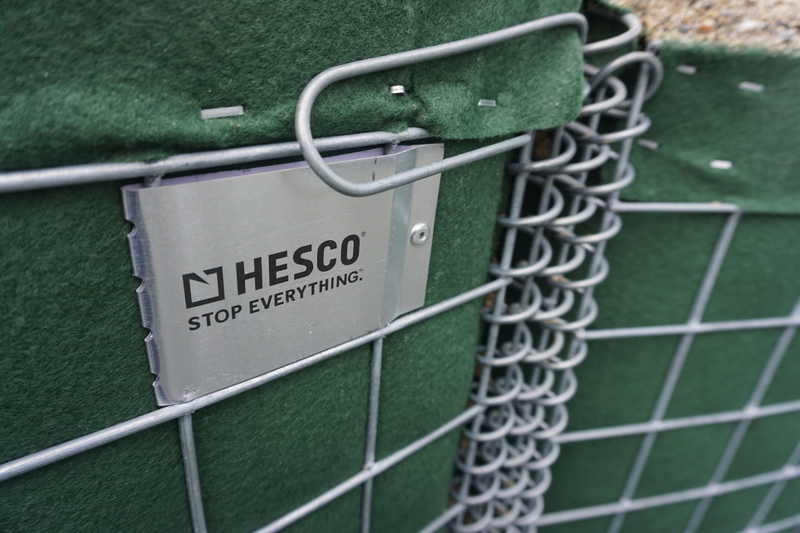 A military-grade barrier, seen May 14, 2025, lines the Mendenhall River in the neighborhood inundated by the record 2024 outburst flood from Mendenhall Glacier. The barrier, from a company called HESCO, was recommended by the U.S. Army Corps of Engineers as a temporary protection for the Juneau suburb. (Photo by Yereth Rosen/Alaska Beacon)