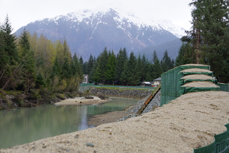 A military-grade barrier, seen May 14, 2025, lines the Mendenhall River in the neighborhood inundated by the record 2024 outburst flood from Mendenhall Glacier. The barrier, from a company called HESCO, was recommended by the U.S. Army Corps of Engineers as a temporary protection for the Juneau suburb. (Photo by Yereth Rosen/Alaska Beacon)