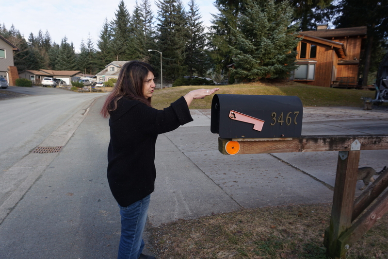 Danielle Lindoff, standing in front of her Mendenhall Valley house on March 13, 2025, shows how high water rose during the record glacial outburst flood of August 2024. On that night, as her husband steered the boat they used to escape, Lindoff held out a flashlight to look for submerged mailboxes so they could avoid bumping into them. (Photo by Yereth Rosen/Alaska Beacon)