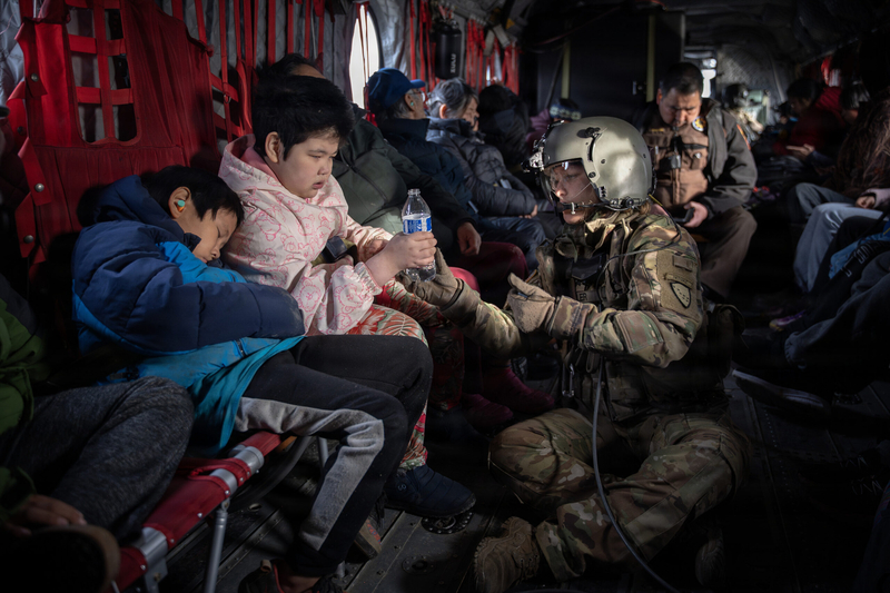 Alaska Army National Guard Sgt. Mary Millerpasses a bottle of water to a child while evacuating displaced residents of Kwigillingok on Oct. 16, 2025. Alaska Army National Guard helicopter aircrews, with the 207th Aviation, pulled residents from Yukon-Kuskokwim Delta communities hit by the remnants of Typhoon Halong and transported them to Bethel for follow-on travel to Joint Base Elmendorf-Richardson in Anchorage. (Photo by Alaska National Guard photo by Staff Sgt. Joseph Moon/Alaska National Guard)