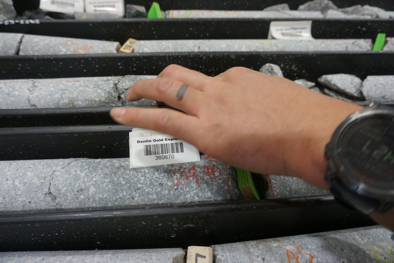 A visitor to the Donlin Gold mine site on June 23, 2025, touches core samples collected from exploration work. (Photo by Yereth Rosen/Alaska Beacon)
