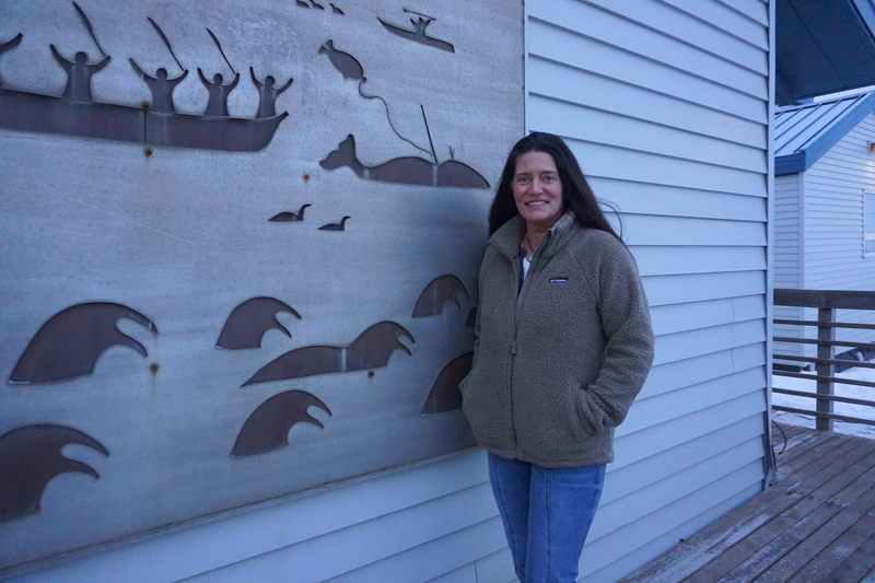 Kathi Lefebvre, a research biologist with the National Oceanic and Atmospheric Administration's Fisheries service, stands by a mural at the University of Alaska Fairbanks' Nome campus on April 9, 2026. Lefebvre, an expert on algal toxins and their effects on marine mammals, is one of the leaders of a research project partnering with Bering Sea tribes. The project is evaluating risks from harmful algal blooms to subsistence food resources; the mural depicts traditional hunts of walruses, seals and whales, wh