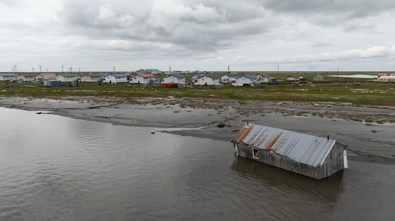 A home sits in the river in Kwigillingok, Alaska, on June 18, 2026. During ex-Typhoon Halong, homes were lifted from their foundations and carried across the tundra and river by floodwaters. Many residents were later airlifted to safety. (Katie Basile for Anchorage Press)