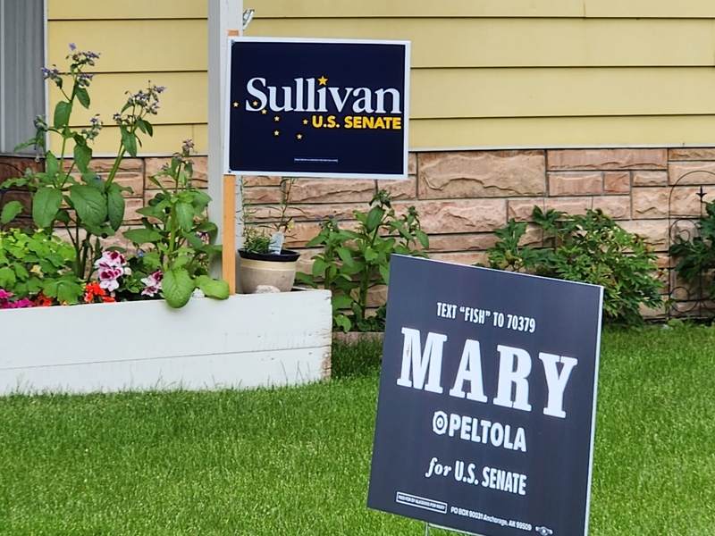Competing signs in the same Midtown Anchorage yard, seen Aug. 7, 2026, support the candidates for U.S. Senate in Alaska: incumbent Dan Sullivan, a Republican, and challenger Mary Peltola, a Democrat. (Photo by Yereth Rosen/Alaska Beacon)