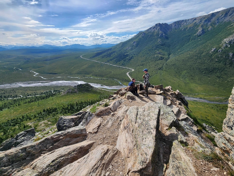 Hikers rest on an outcropping on the Savage Alpine Trail in Denali National Park on July 26, 2026. The sole road through the park is seen below. Travel restrictions on the 92-mile park road begin at the 15-mile mark, at the Savage River, seen in the background. (Photo by Yereth Rosen/Alaska Beacon)