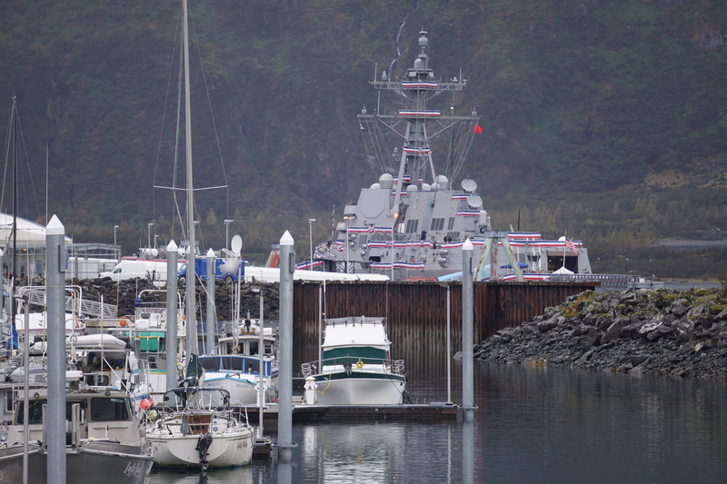 The USS Ted Stevens, a new U.S. Navy warship, towers over boats in Whittier's small harbor on Oct. 1, 2026. (Photo by Yereth Rosen/Alaska Beacon)