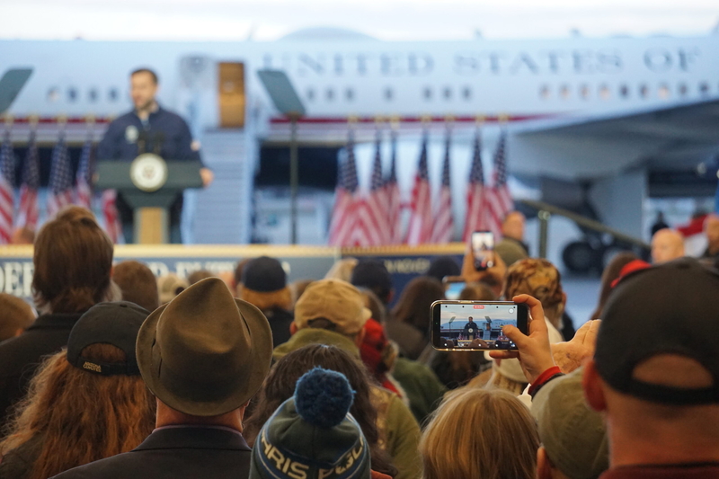 A rally attendees records Vice President JD Vance as he speaks in Fairbnks on Oct. 5, 2026. Vance was in Fairbanks to campaign for U.S. Sen. Dan Sullivan, R-Alaska. The event drew hundreds of people to the venue, an airport hangar. (Photo by Yereth Rosen/Alaska Beacon)