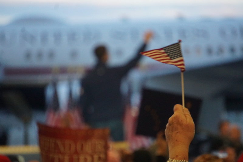 An attendee holds up a small American flag as Vice President JD Vance returns to Air Force 2 after delivering a campaign speech in Fairbanks on Oct. 5. Vance came to Fairbanks to campaign for U.S. Sen. Dan Sullivan, R-Alaska. (Photo by Yereth Rosen/Alaska Beacon)
