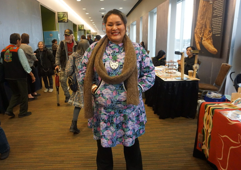 State Rep. Nellie Jimmie, D-Toksook Bay, stands in a corridor at the Dena'ina Civic and Convention Center in Anchorage on Oct. 24, 2026, during the ALaska Federation of Natives convention. She is dressed in a traditional kuspuk and wearing a scarf she knitted from qiviut, the soft and ultra-warm hair found on muskoxen. She hunted the musk ox as well, she said. The Arctic fox jewelry necklace she is wearing was made by a niece, she said. (Photo by Yereth Rosen/Alaska Beacon)