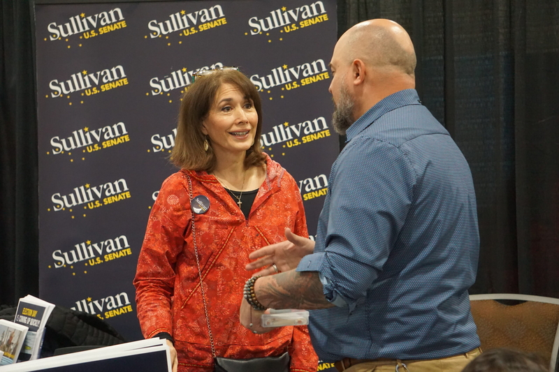 Julie Fate Sullivan, the wife of U.S. Sen. Dan Sullivan, R-Alaska, speaks to a supporter on Oct. 24. 2026, at the art fair set up at the Alaska Federation of Natives convention in Anchorage. The fair, which includes information booths as well as artists' work, is a regular feature of the annual convention. Sullivan is running for re-election, and his wife manned a campaign booth during the convention. (Photo by Yereth Rosen/Alaska Beacon)