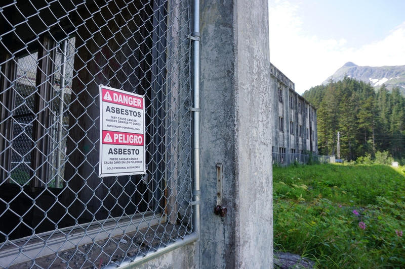 A sign on a fence at the Buckner Building in Whittier, seen Aug. 5, 2024, warns about the presence of cancer-causing asbestos. (Photo by Yereth Rosen/Alaska Beacon)