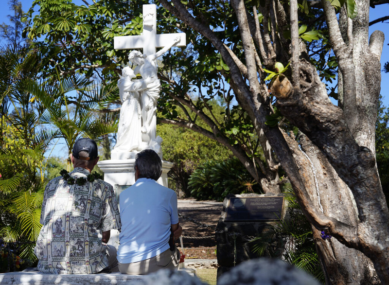 Seawind Tour &amp; Travel founder and CEO Randy King, left, and Sister Alicia Damien Lau sit in front of Mother Marianne’s grave during a Kalaupapa Saints Tour Thursday, Sept. 18, 2025, in Kalaupapa. Sister Alicia of the Sisters of St. Francis of the Neumann Communities belongs to the same community as Mother Marianne. She was canonized as Saint Marianne Cope in 2012 for her work at Kalaupapa. (Kevin Fujii/Civil Beat/2025)