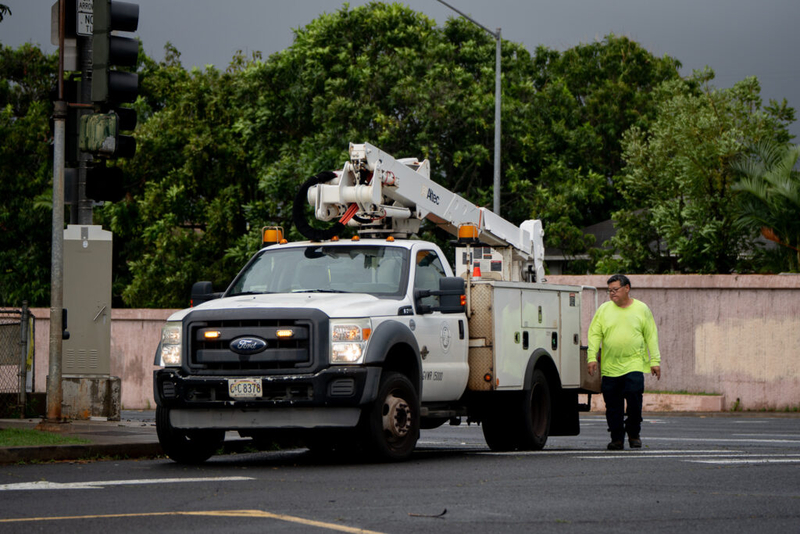 A City &amp; County worker walks next to white bucket truck. The man wears a neon yellow shirt.
