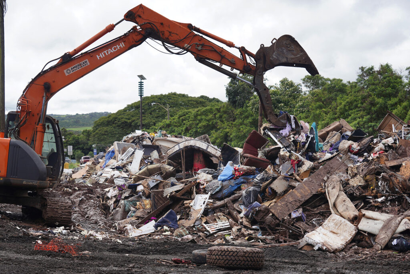 Rubbish is piled into the middle of the traffic circle Monday, March 23, 2026, in Waialua. The traffic circle has become a make-shift refuse transfer center for nearby homes affected by the Kona Storm flooding. (Kevin Fujii/Civil Beat/2026)