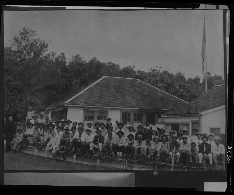 Black and white historical photo of leper patients in front of white houses.
