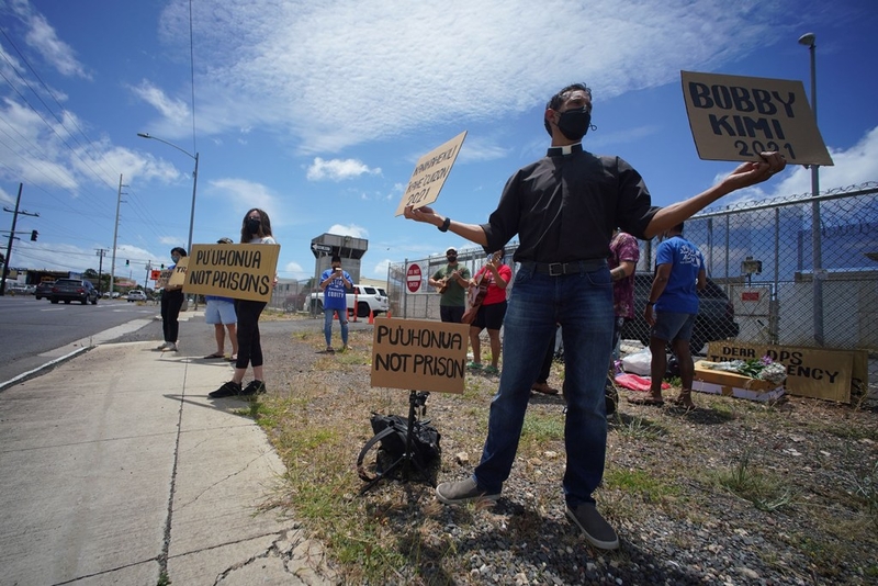 Reverend Brandon Duran holds signs fronting the Oahu Community Correctional Center OCCC.