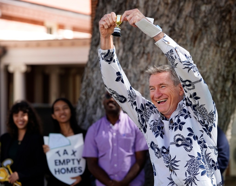 Honolulu Council Chair Tommy Waters hoists his Empty Homes Tax champion trophy bestowed upon him during a University of Hawaii sponsored news briefing to support the Empty Homes Tax Thursday, Nov. 21, 2024, in Honolulu. (Kevin Fujii/Civil Beat/2024)