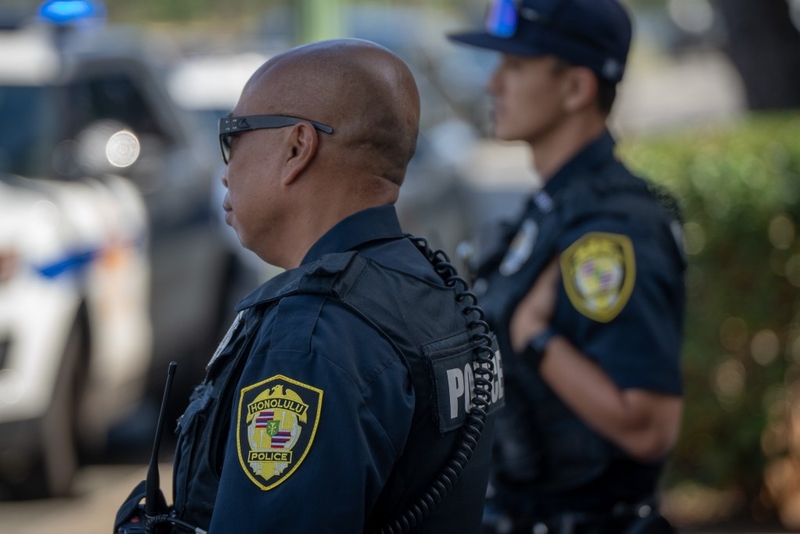 Honolulu Police officers wearing dark uniforms looking to the left. The department’s logo is seen on the officers’ left sleeve.
