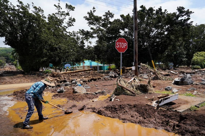 A resident who wished to be identified as Na Wahine Koi shovels mud from the intersection of Hawaiʻi Belt Road and Kaʻalaiki Road in the town of Nāʻālehu Tuesday, Aug. 18, 2026, on Hawaiʻi Island. Hurricane Lala made a close pass to the South Point of the Big Island Saturday. (Kevin Fujii/Civil Beat/2026)