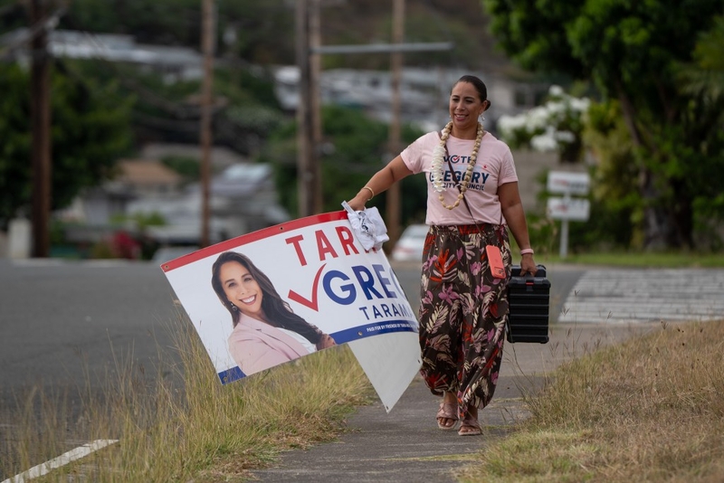 District IV council candidate Tara Malia Gregory carries a campaign sign to a sign waving site in Hawaiʻi Kai August 5, 2026. (Craig Fujii/Civil Beat/2026)