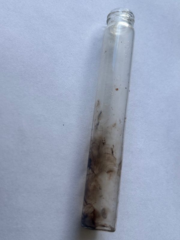A small cylindrical glass pipe with the bottom half stained black from smoke.