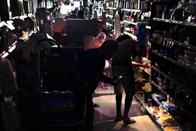 Using smartphone flashlights, grocery store customers shop for necessary items in the dark Wednesday, Sept. 9, 2026, in Kapaʻa. A customer near the front of the line said he had been in line to check out for two hours. (Kevin Fujii/Civil Beat/2026)