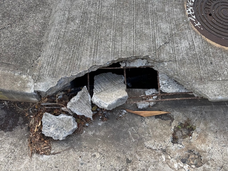 concrete crumbles around a hole in the sidewalk