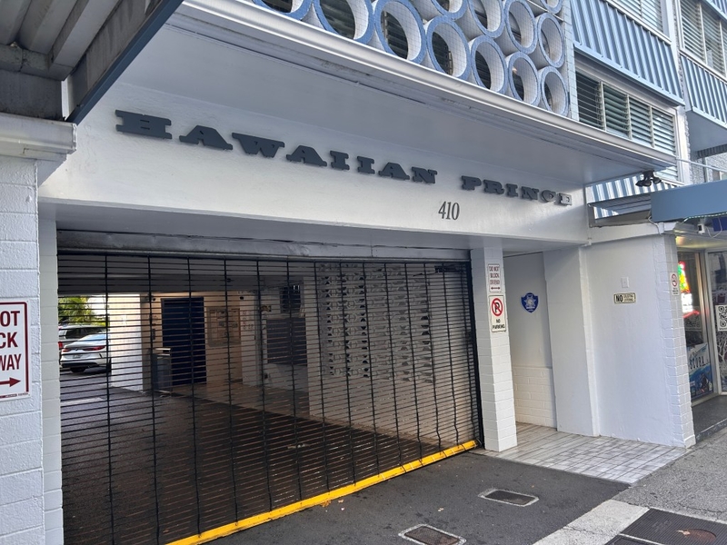 A metal roller gate is shown left on the ground floor of a building with the name and number of the building displayed above the driveway.