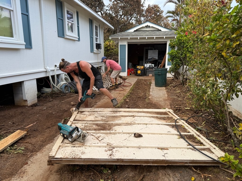 Christian Roman (left) cuts part of a wooden fence pushed by ocean waves from the house across the street while his twin brother, Evan, picks up a piece of lattice. Hurricane Lowell caused 20- to 30-foot waves to pummel beachfront houses along Ho‘ona Road in Po‘ipū. (Noelle Fujii-Oride/Civil Beat/2026)