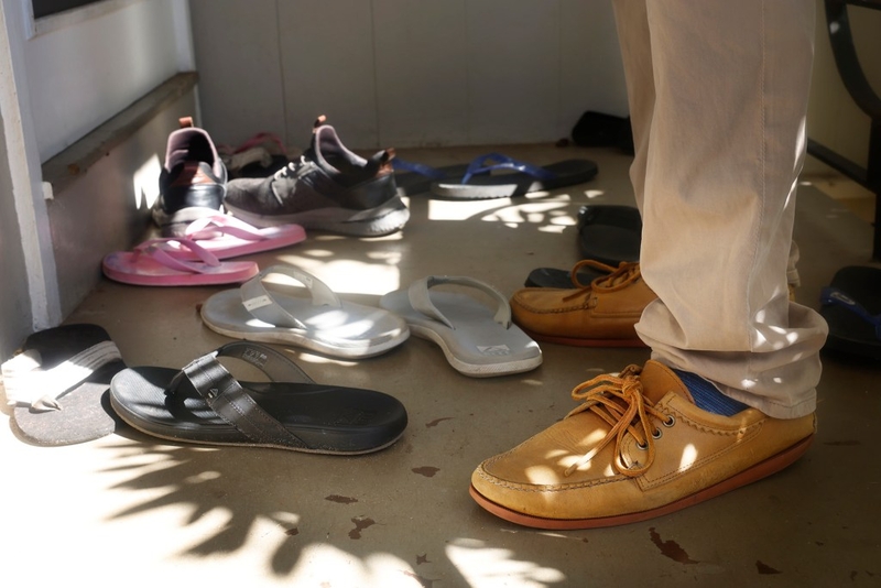 You know you’re campaigning in Hawaiʻi when council candidate Trevor Ozawa has to straddle slippers and shoes outside a Kāhala home Wednesday, Oct. 14, 2026, in Honolulu. (Kevin Fujii/Civil Beat/2026)