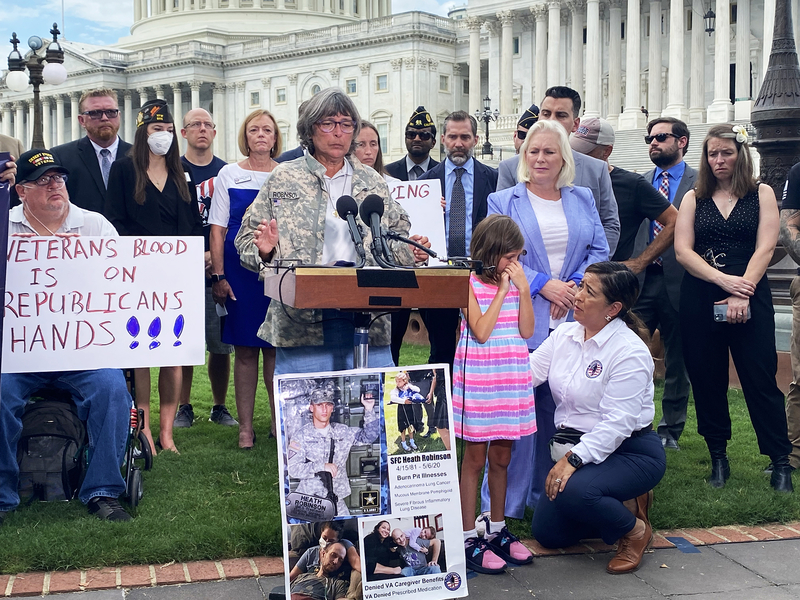 Susan Zeier, mother-in-law of late Sgt. First Class Heath Robinson of the Ohio National Guard, speaks during a news conference on the PACT Act on July 28, 2022, while Rosie Torres, co-founder of Burn Pits 360, comforts Robinson's daughter, Brielle Robinson. (Jennifer Shutt/States Newsroom)