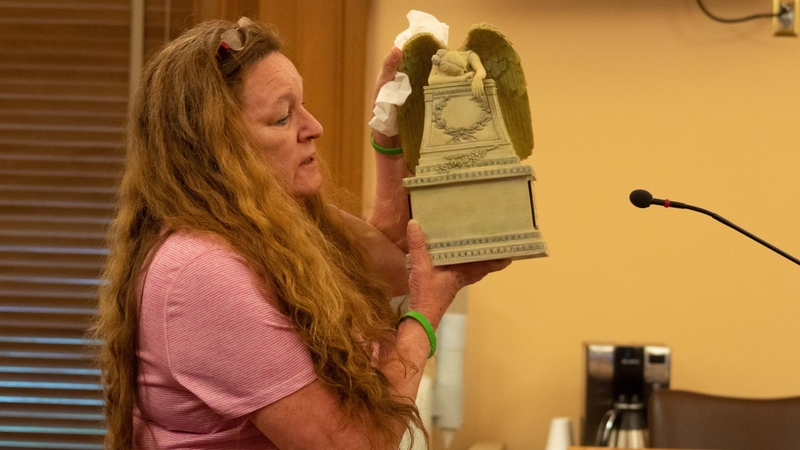 Sherry Lesher holds up her son's urn while speaking at a podium