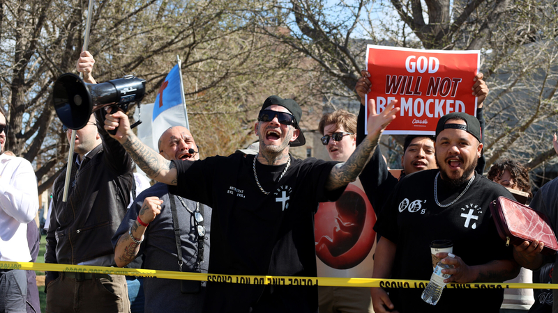 The Cure Church member Daniel Casteel, center with megaphone, was among Christians who used amplified equipment Friday outside the Kansas Capitol to broadcast their invitation for people to renounce Satan and welcome Jesus into their lives. He bellowed to his target audience a law enforcement barrier: "Any time you're ready, you can step this way. We will make sure you get saved. Come give your life to Jesus." (Grace Hills/Kansas Reflector)