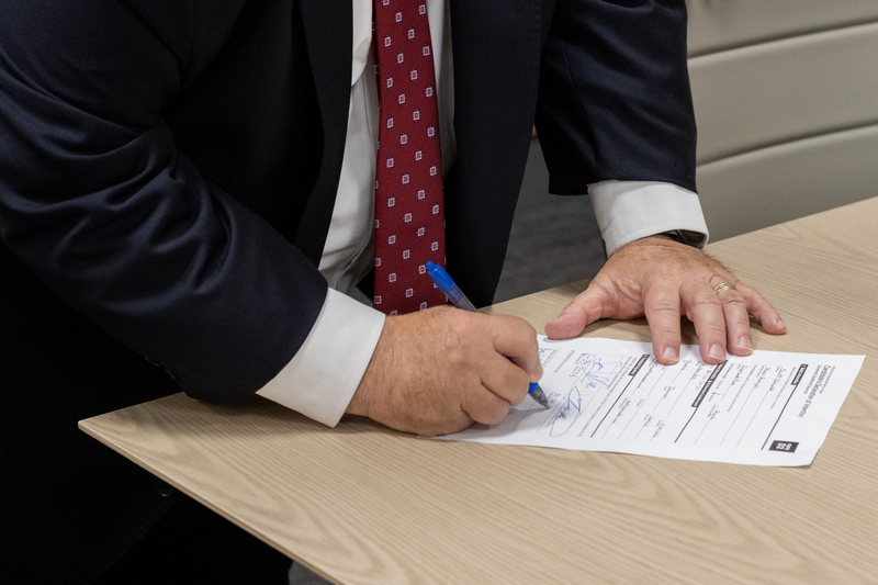 A man in a suit signs a document in blue ink