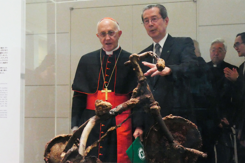 Chair Yasuyoshi Komizo stands with Cardinal Fernando Filoni at the peace museum at Hiroshima, Japan, in 2017. Komizo is discussing a tricycle scorched by the Aug. 6, 1945, atomic bombing of the city.