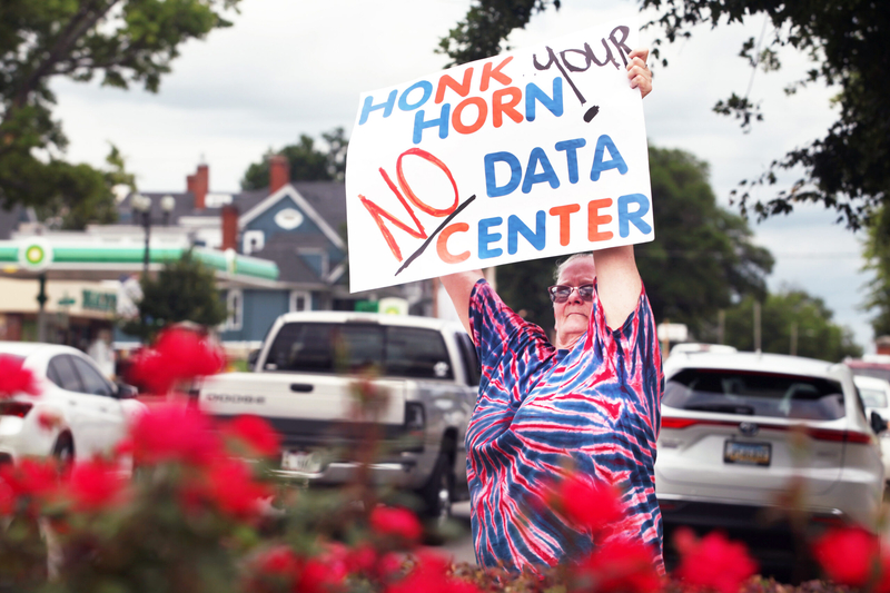 Data center protestor Sherrie Kennison waves a sign at passing traffic on June 23, 2026, outside the Emporia city offices.