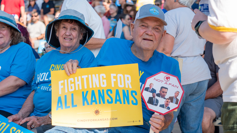 Archie Blumhorst, the father of Cindy Holscher, holds signs supporting the candidate on Sept. 12, 2026, at the Kansas State Fair in Hutchinson.