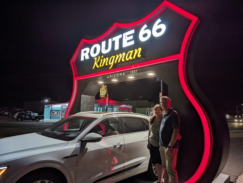 Thomas Wischgoll and his wife, Rosa, pose with their electric vehicle at the Route 66 drive-through sign in Kingman, Arizona.