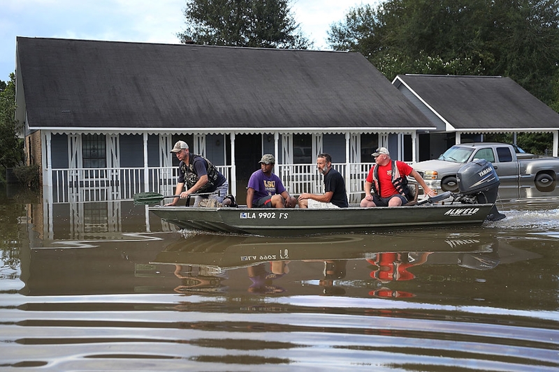 A man navigates a boat with three passengers past a flooded home.