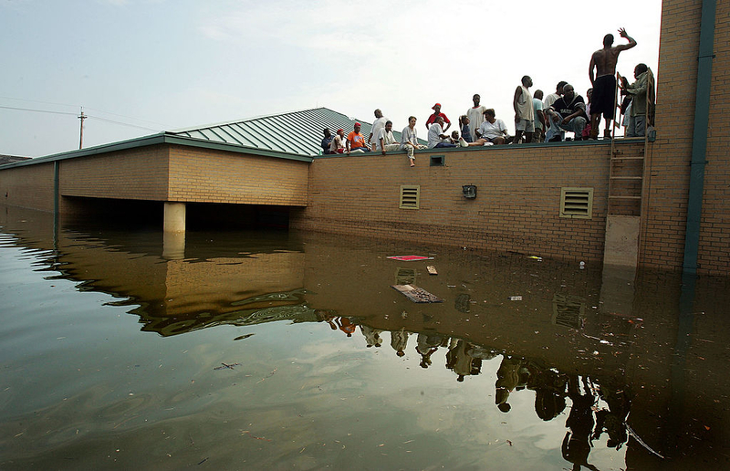 People escape flooding in the Lower 9th Ward and wait to be rescued from the rooftop of the Martin Luther King Jr. School and Library, one of the only two-story buildings in the area, during the aftermath of Hurricane Katrina Aug. 30, 2005 in New Orleans.