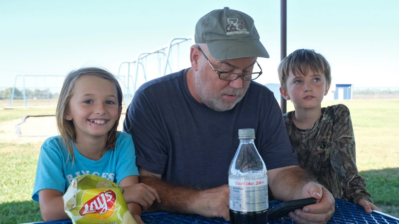 Penelope Hull, her grandfather Randy Ogles, and brother Lucien Hull sit at a picnic bench