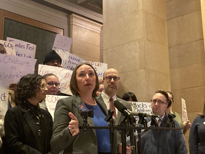 Minnesota state Rep. Carlie Kotyza-Witthuhn speaks at a podium with supporters holding signs behind her at a Dec. 31, 2025, news conference.