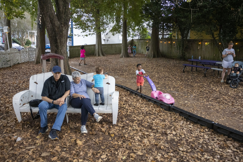 An elderly couple sits on a bench while children play at Confetti Playspot in Algiers Point